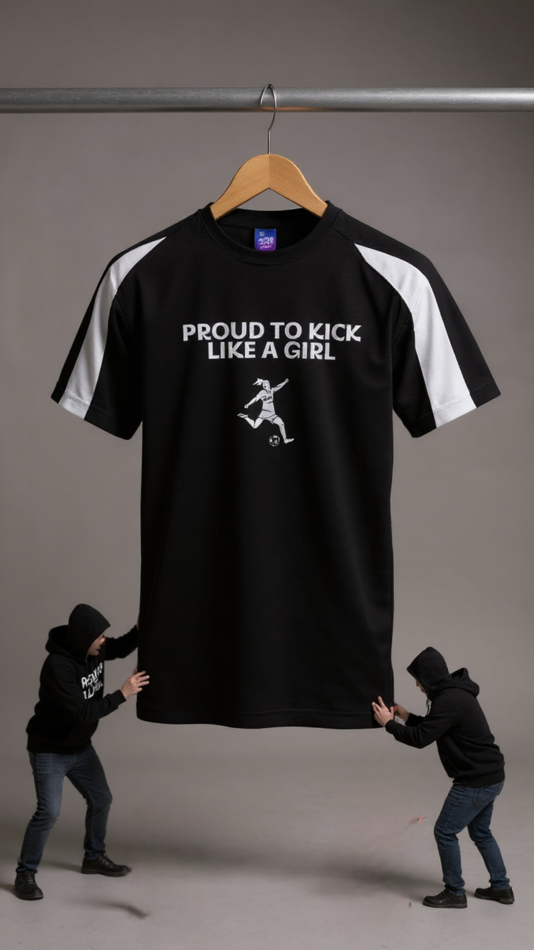 Black t-shirt with 'Proud to Kick Like a Girl' text and graphic on a hanger, with two people holding it.